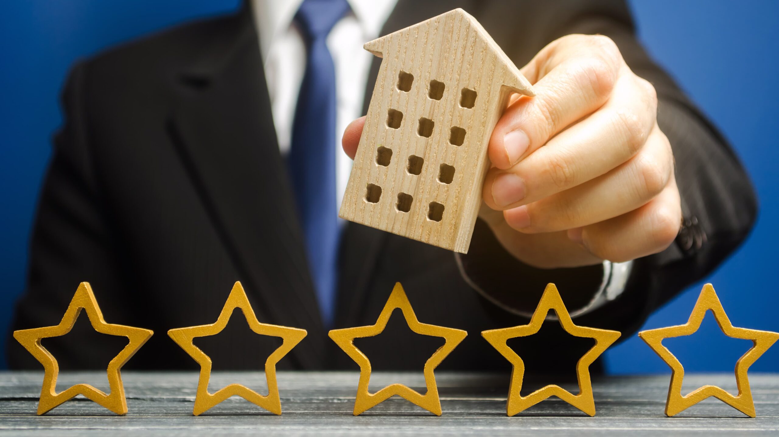 Ein Geschäftsmann hält ein Hotelsymbol über fünf Sternen in der Hand, um auf die positiven Bewertungen und hohe Kundenzufriedenheit seines Hotels hinzuweisen. Ein dauerhaftes und Marketing